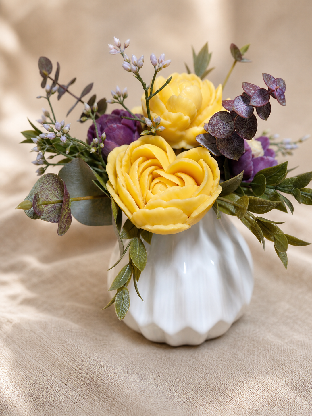 Yellow scented wax rose arrangement with plum accents and greenery in a white fluted vase